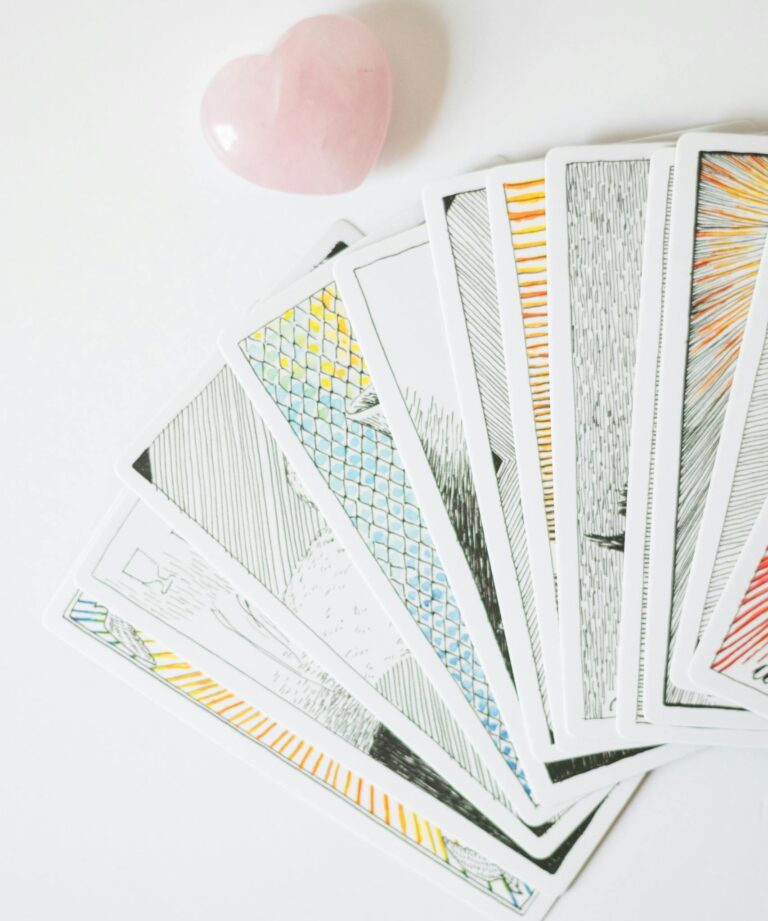 A spread of tarot cards fanned out on a white background with a heart-shaped stone.