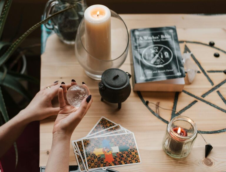 From above of crop unrecognizable female soothsayer with magic ball near tarot cards and candles during divination process in house