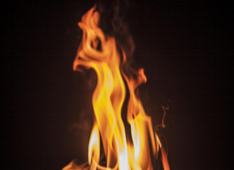 Intense close-up shot of vibrant flames engulfing firewood against a dark background.