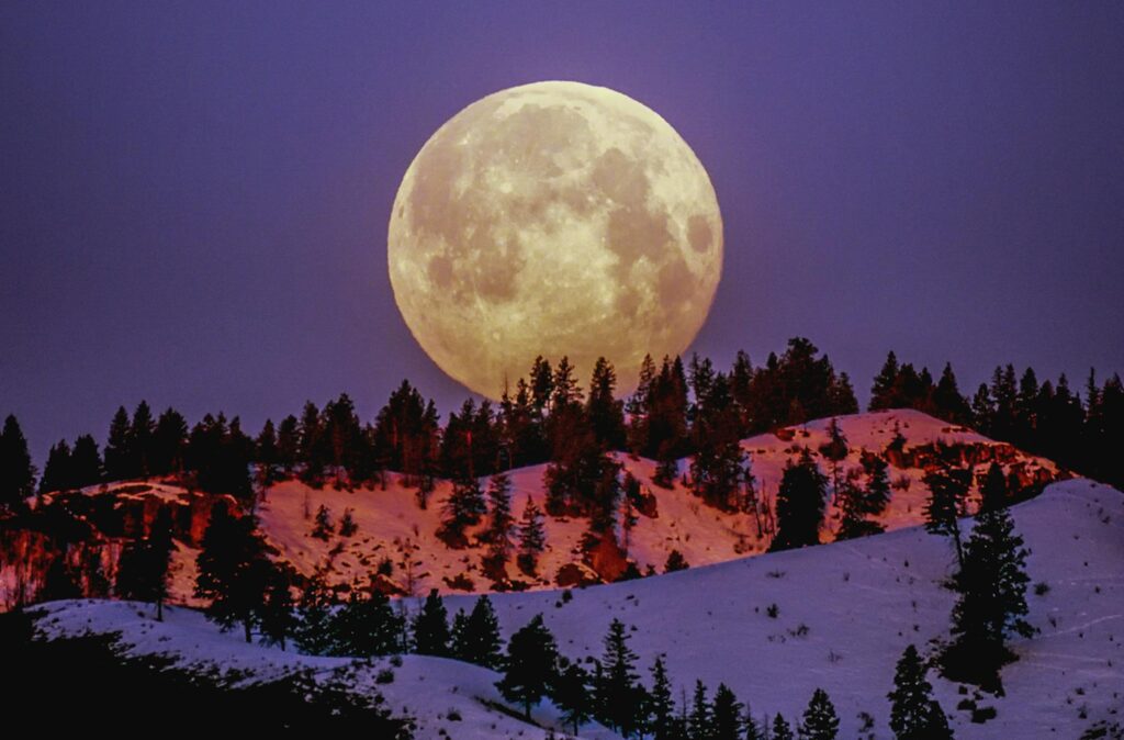 A breathtaking supermoon illuminating snow-covered hills under a purple sky in Wenatchee, WA.