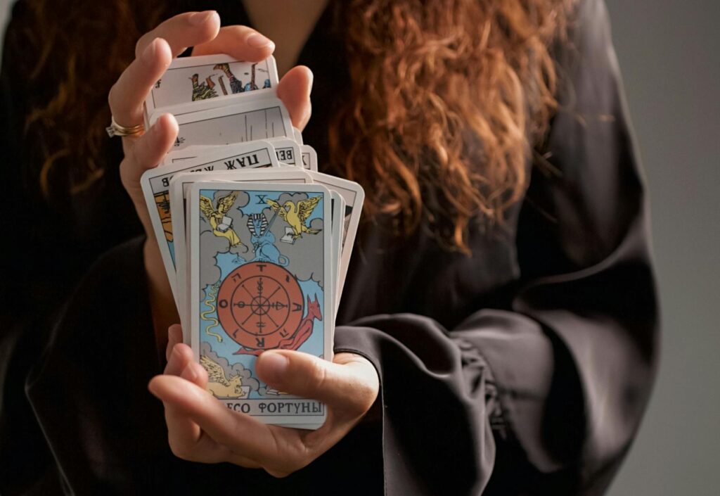 Close-up of a woman in black dress holding tarot cards, symbolizing spirituality and divination.